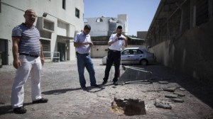 Israelis look at a crater caused by a rocket outside a shop in Ashdod, on the second day of Operation Protective Edge, Wednesday, July 9, 2014 (photo credit: Yonatan Sindel/Flash90 